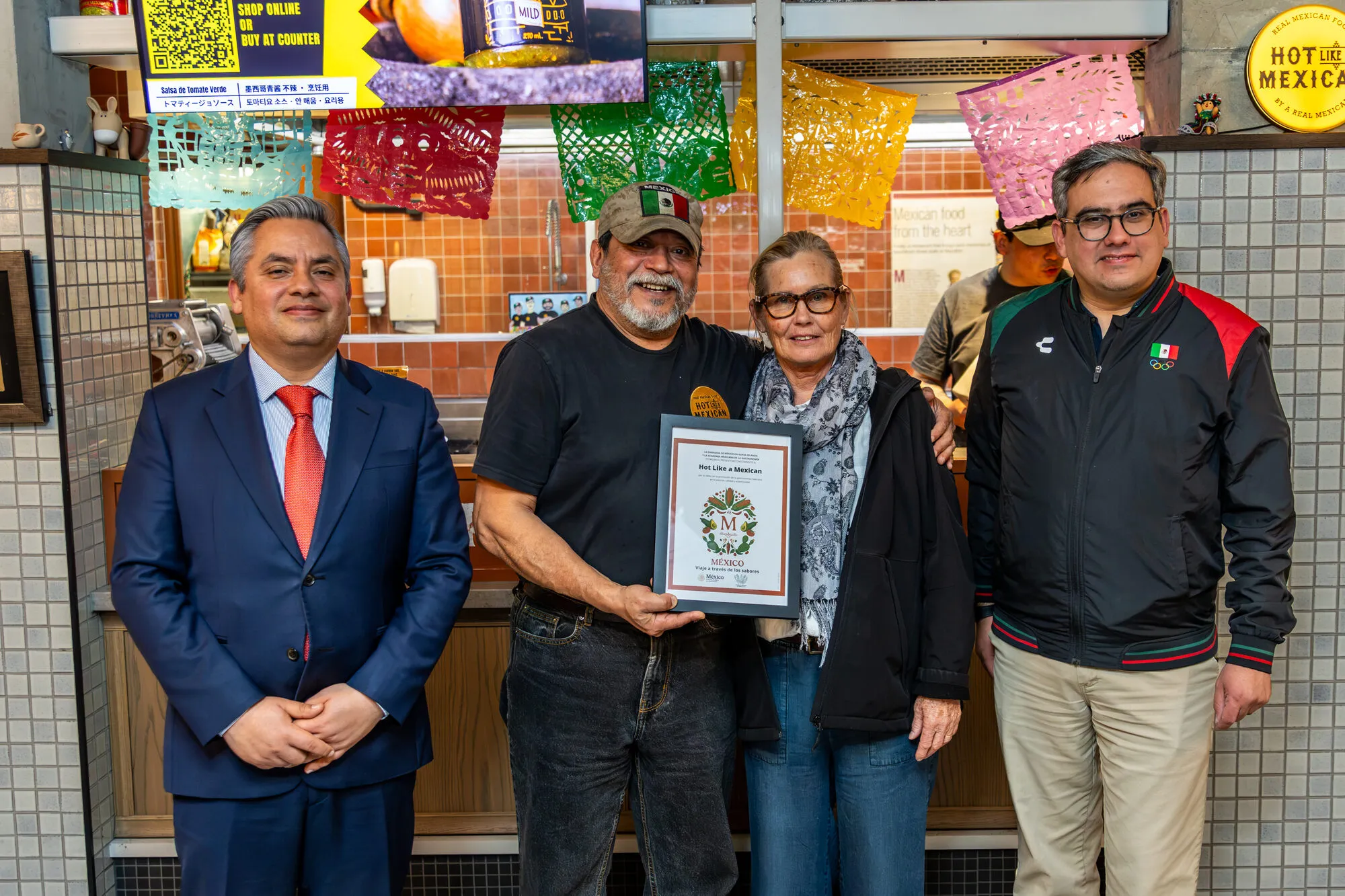 Carlos Rubio and Pedro Ludwig Barragán Garza of the Embassy of Mexico stand either side of Andrés Pimentel, who holds the Sello M certificate, at the Hot Like a Mexican counter