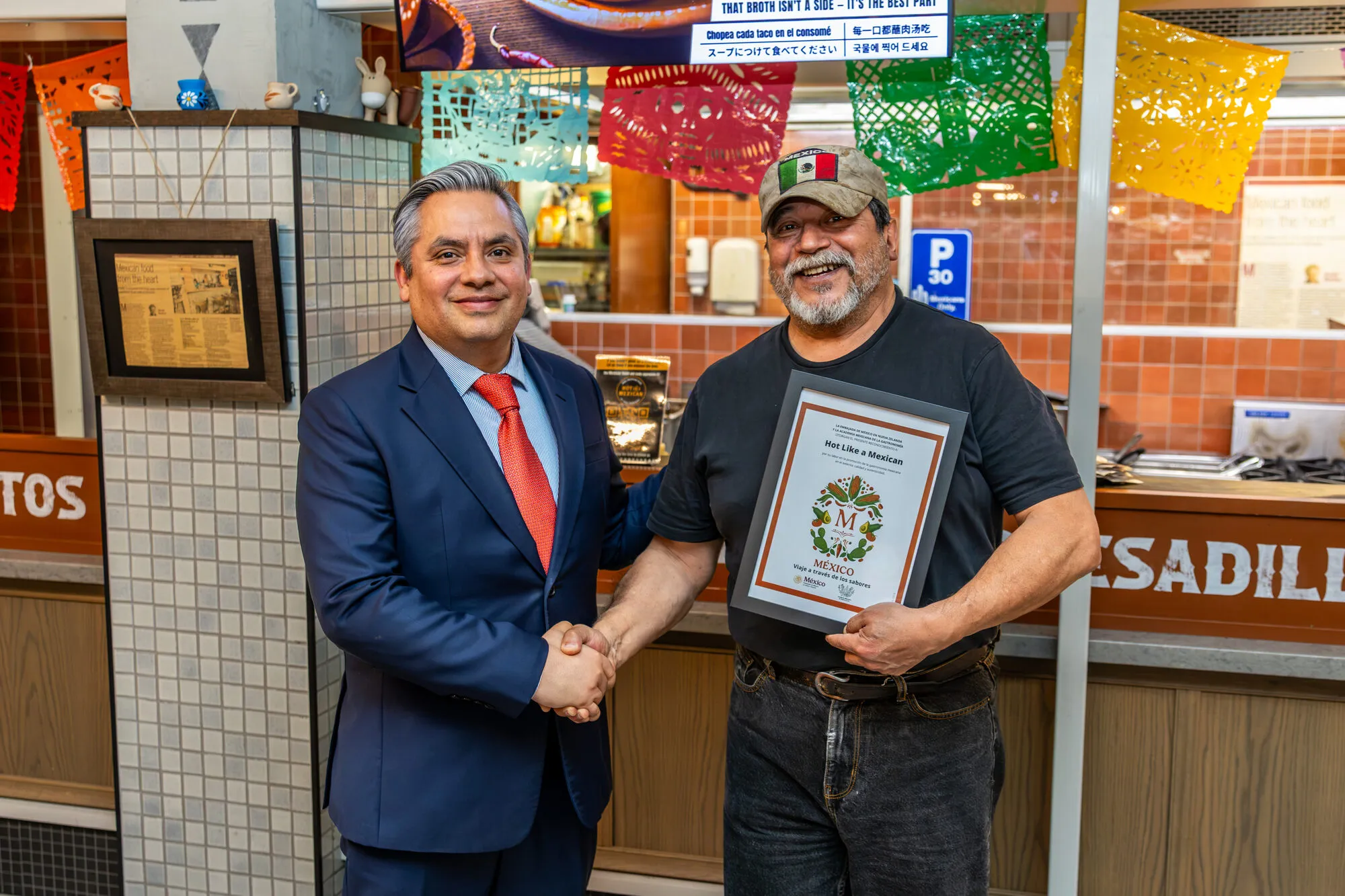Carlos Rubio of the Embassy of Mexico shakes hands with Andrés Pimentel, who holds the framed Sello M certificate